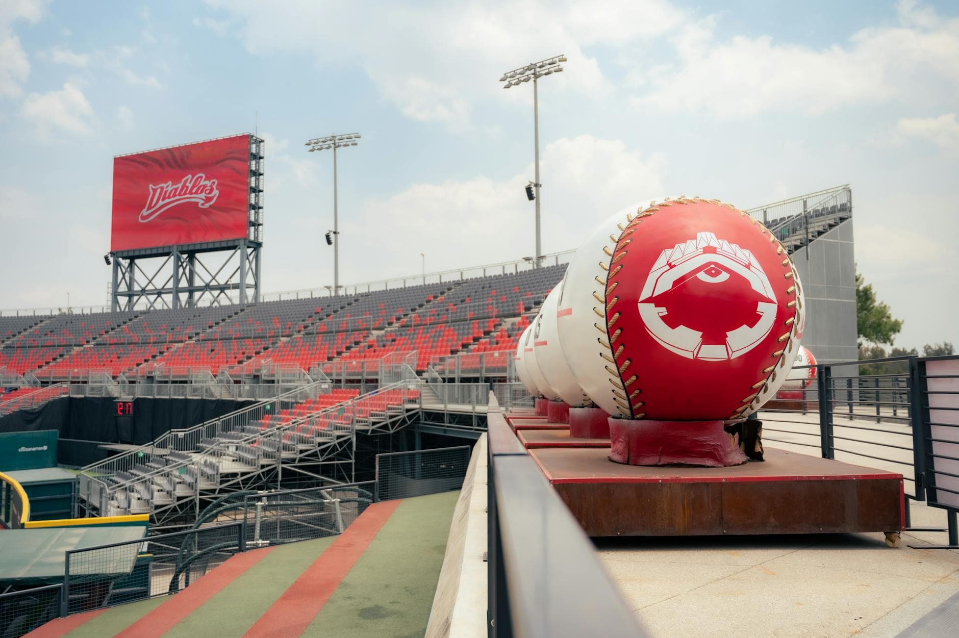 A view of an empty stadium with oversized baseball decorations under a clear sky.