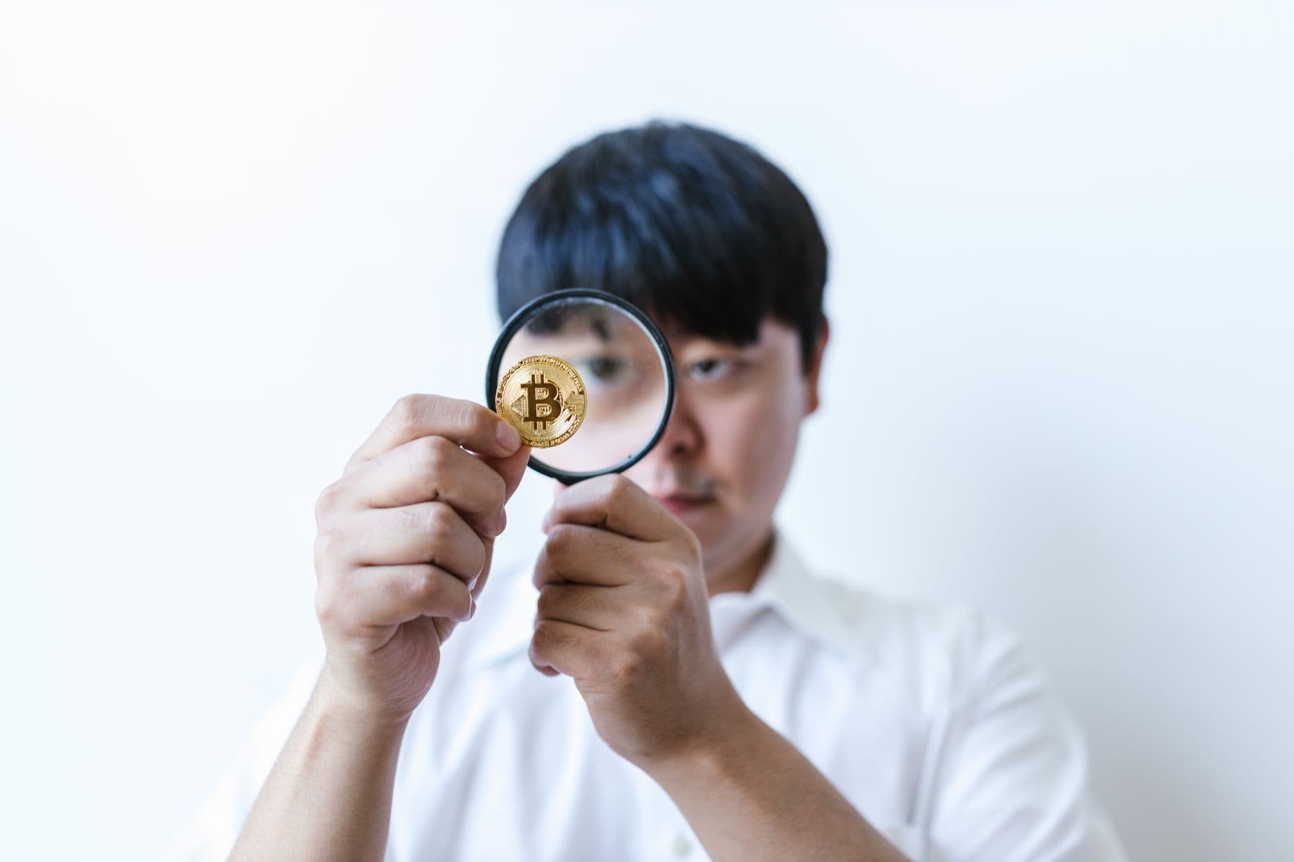 Close-up of a man examining a Bitcoin coin with a magnifying glass, symbolizing cryptocurrency analysis.