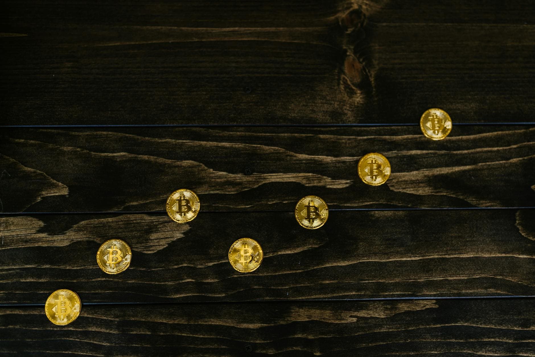 Gold-colored bitcoins arranged diagonally on a dark wooden surface.