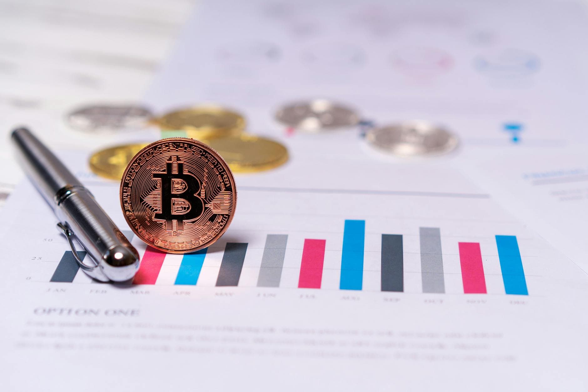 Close-up of a Bitcoin coin placed on financial charts with a pen, symbolizing cryptocurrency and economic analysis.