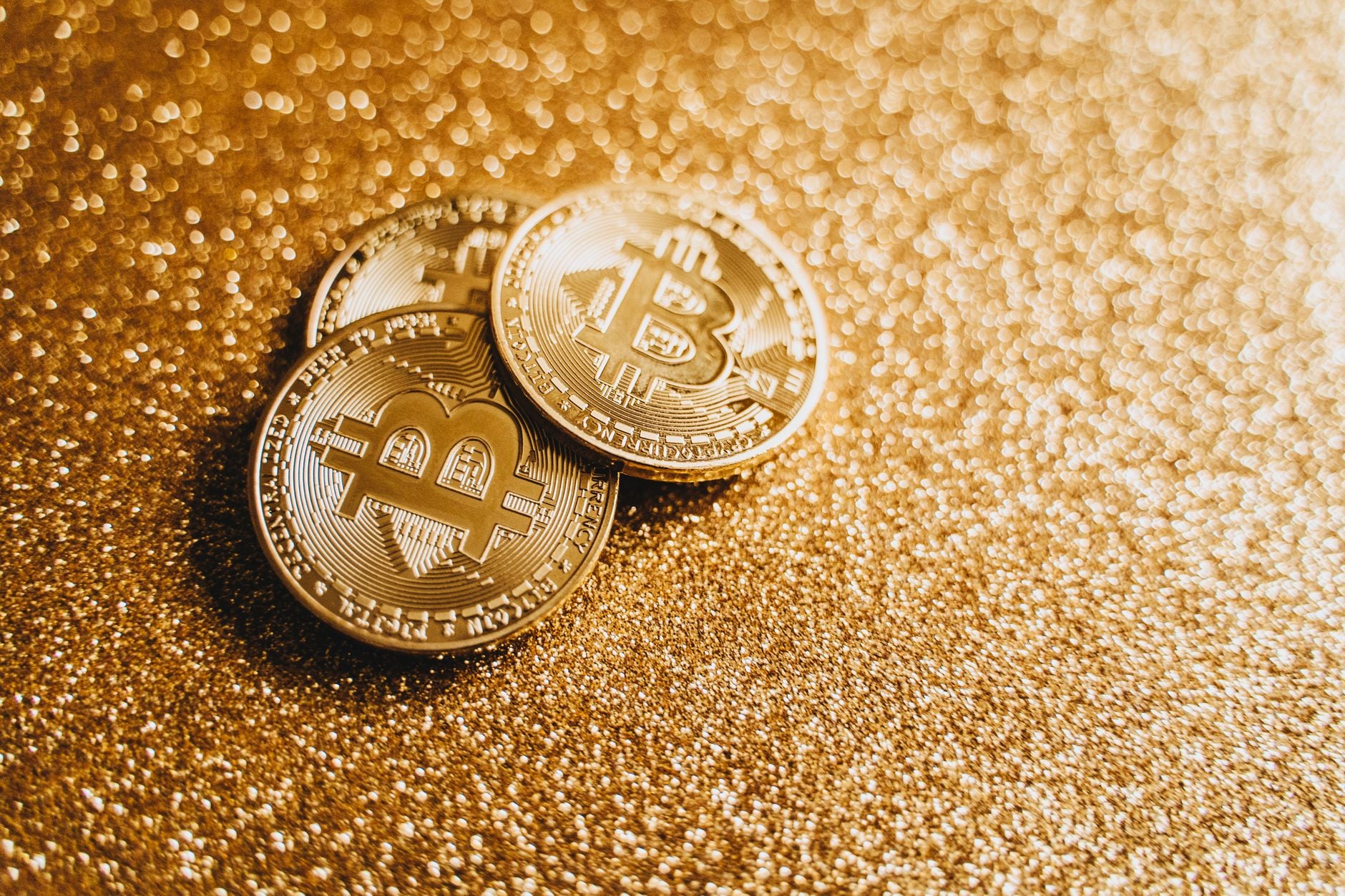Closeup of three Bitcoin coins on a shimmering gold glitter background, symbolizing digital wealth.